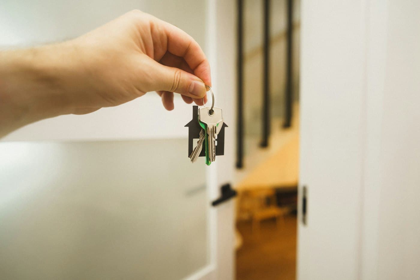 A hand holding a house key by an open front door